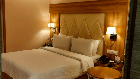 A Bharuch hotel room featuring a neatly made bed, bedside lamps, and a decorative headboard in Rang Lords Inn Bharuch