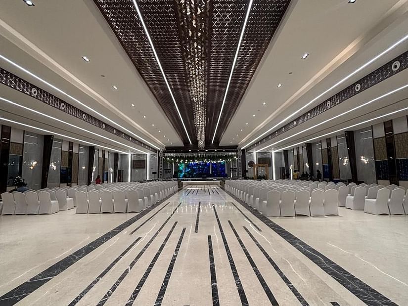 Elegant indoor banquet hall with decorative ceiling panels, modern lighting, and rows of white-covered chairs facing a stage - VRR Astoria Hotel & Convention Centre.