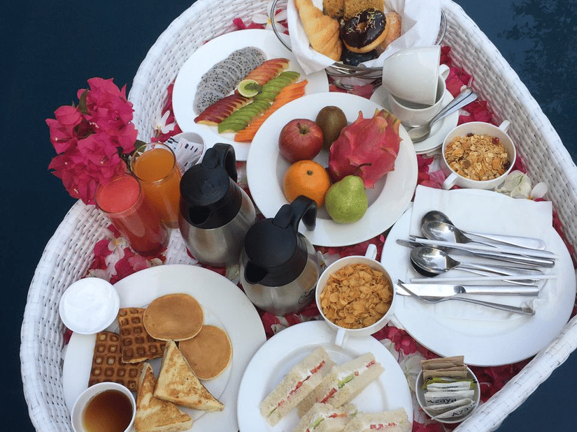 A white heart-shaped floating tray filled with small dishes of fruit salad and breakfast items.