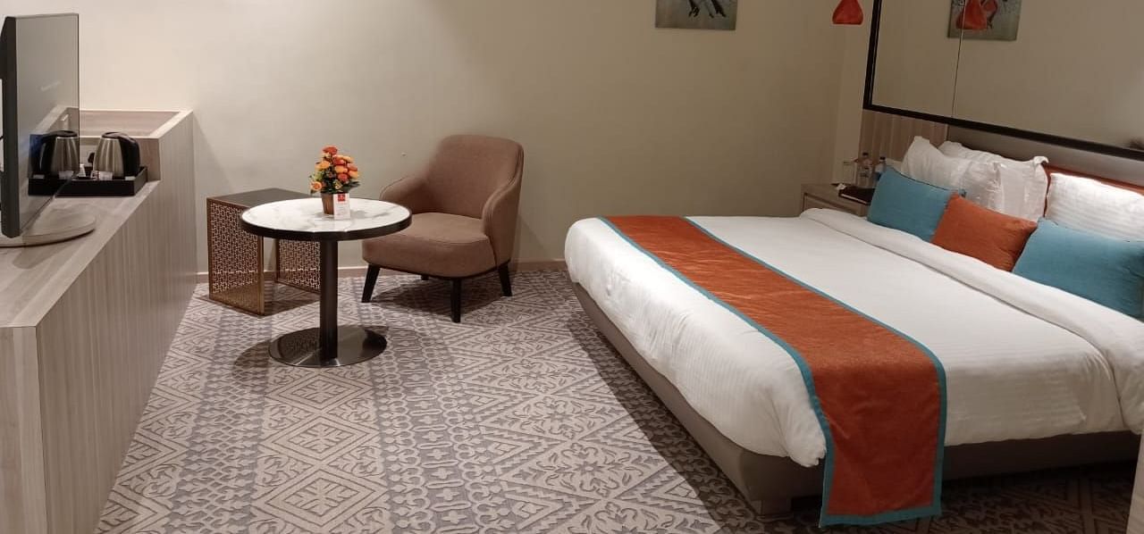 Modern hotel room with twin beds, a small table and chair, soft lighting, and minimalist decor.