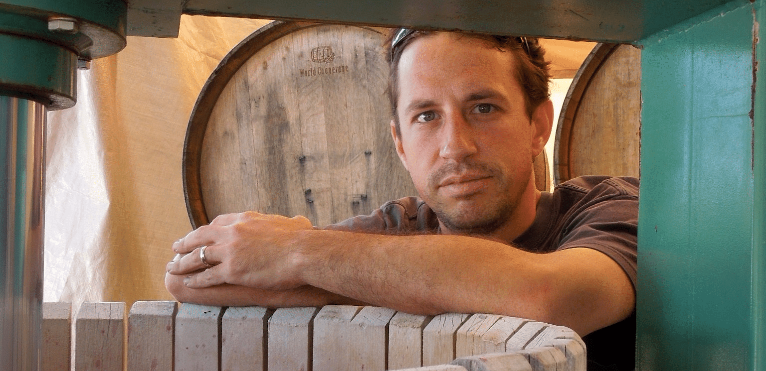 Wooden barrels are stacked and a man standing beside it.
