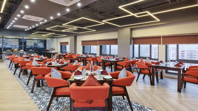 Large indoor restaurant area with vibrant orange chairs and geometric lighting - Pride Elite Gandhinagar
