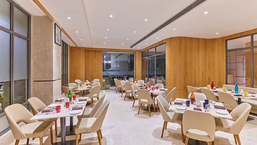Pride Cafe at Biznotel by Pride Motera, Ahmedabad featuring interior with beige chairs, wooden walls, marble flooring, and neatly set tables, brightly lit with ceiling lights.