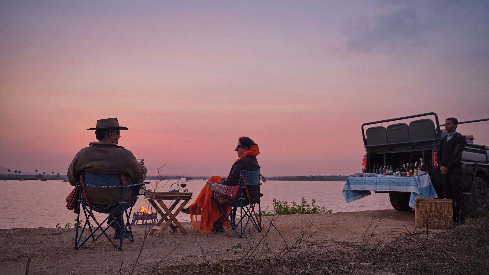 couple soaking in the pink hues of the sunset with a picturesque lake in front of them at dev shree , deogarh