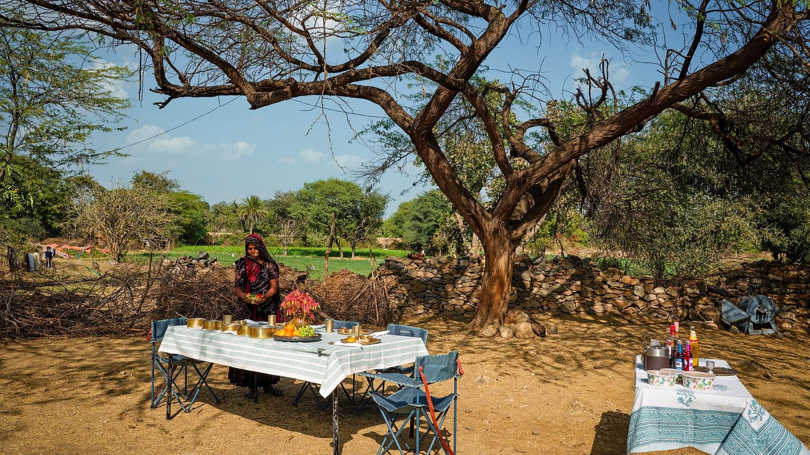 image of a woman dressed in traditional outfit serving various rajasthani delicacies on the table at dev shree, deogarh
