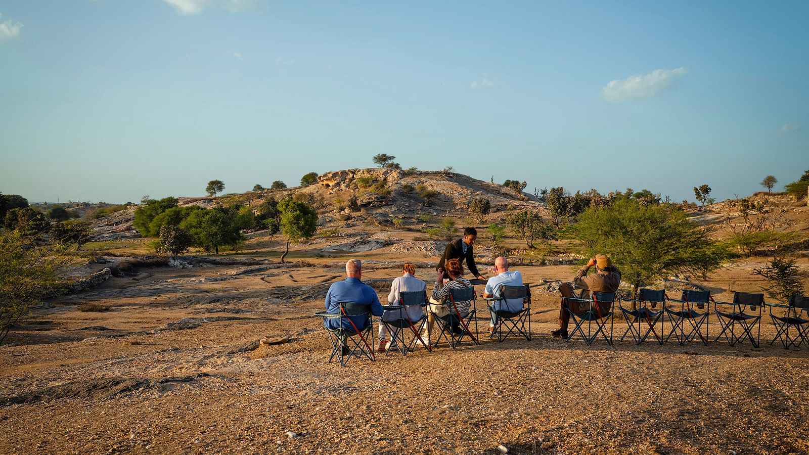 image of a few people sitting on chairs lined up in a rocky desert like area with very less green cover