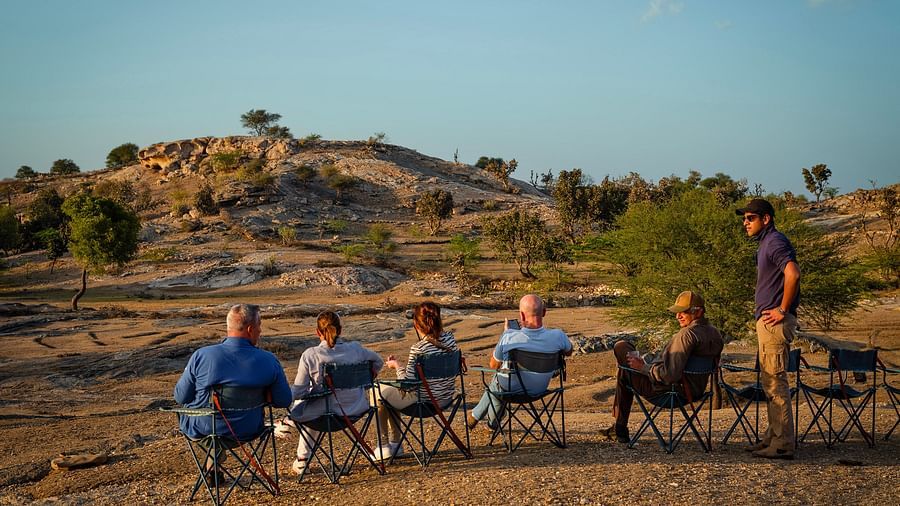 image of a few people sitting on chairs lined up in a rocky desert like area with very less green cover