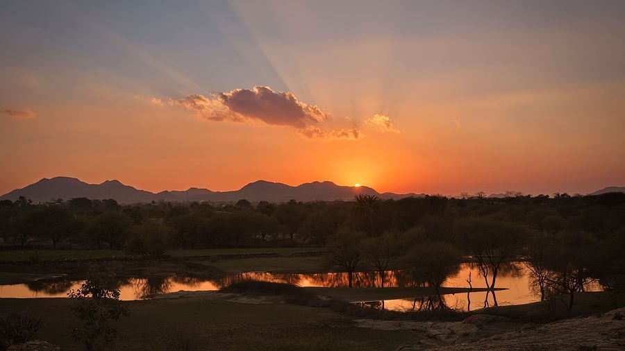 image of a beautiful sunset behind the aravalli range with a lake in the foreground witht he reflecction of the sunset
