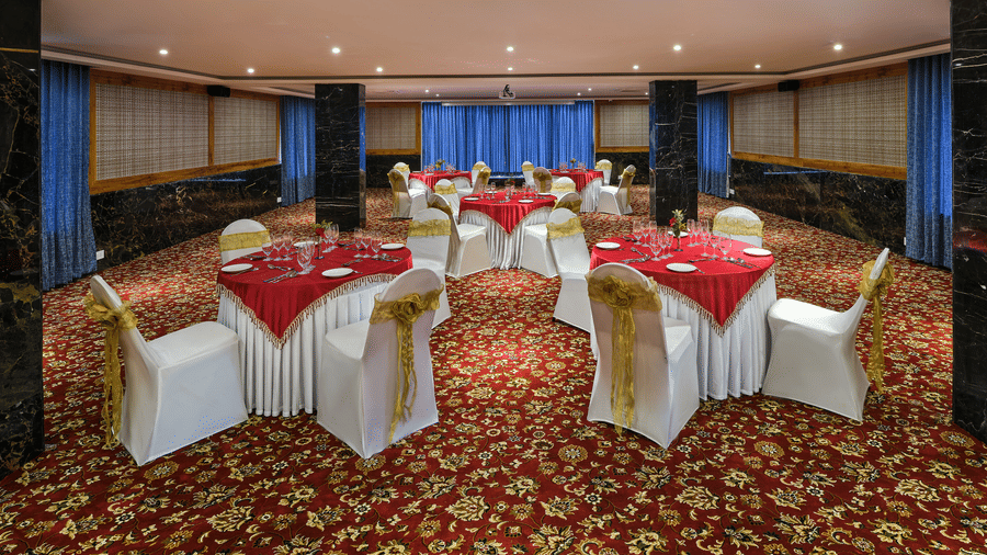 Seating arrangement in the Carnival banquet hall at Essentia Premier Hotel, Chennai featuring several table surrounded by 4 chairs around a round table in between them each.