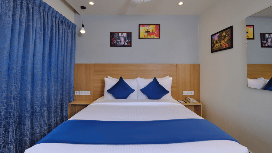 An overview of the Standard Room with a double bed, paintings above the bed and a ceiling fan at Essentia Premier Hotel, Chennai.