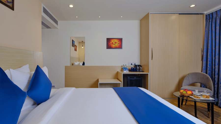 A tidy hotel room in Thoraipakkam with a large bed, blue accents, a wardrobe and a small seating area -Essentia Premier Hotel, Chennai