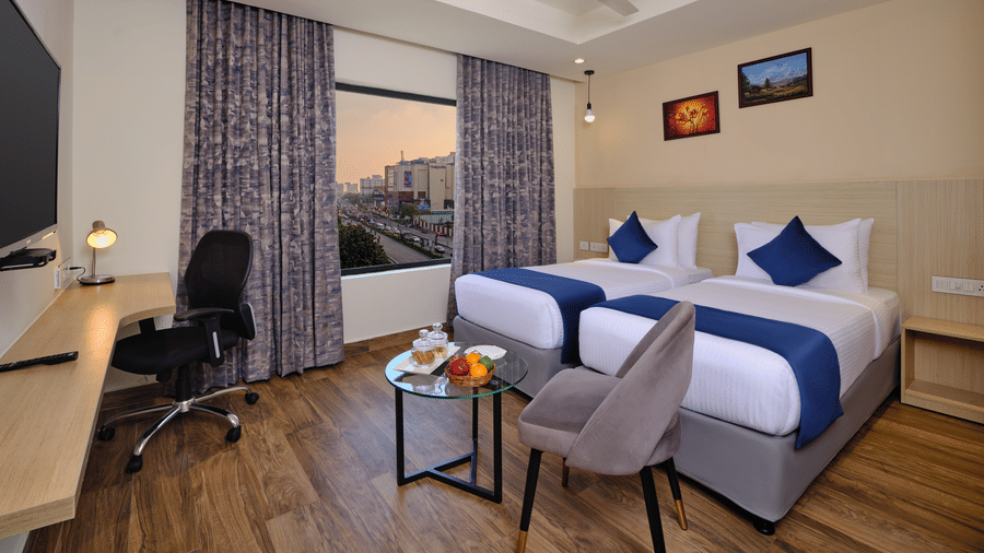 A well-furnished twin room with wooden flooring, a work desk, and a balcony view at our rooms in Thoraipakkam - Essentia Premier Hotel, Chennai