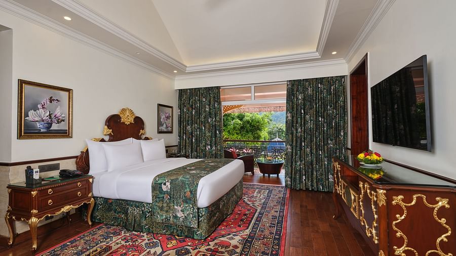 a Family Room bedroom with a large bed on a decorative rug, wooden cabinet, TV, artworks, and a window overlooking greenery 