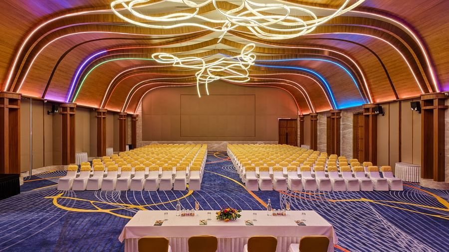 Image of the meeting hall Boito Voyage at Swosti Premium Beach Resorts in Puri featuring a large sitting area for audience under warm lighting and four chairs arranged with a large table facing the audience