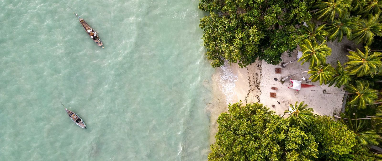 A view of people kayaking in the turquoise waters near a serene beach, surrounded by lush tropical greenery. The peaceful environment adds to the natural beauty of the scene - Coral Reef Resort & Spa, Havelock