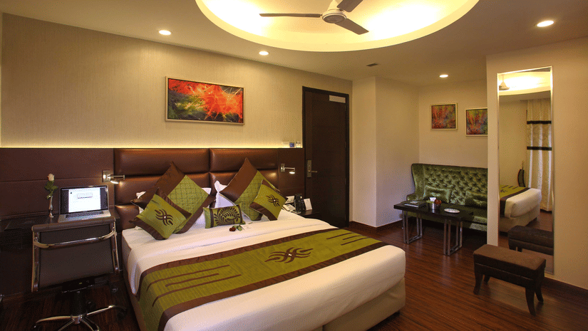 The Club Room at JRD Exortica with a double bed, wooden flooring, a ceiling fan, and modern furnishing.