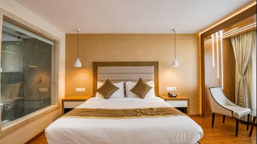 A spacious hotel room with a large bed, elegant seating area by the window, and lighting creating a relaxing ambience