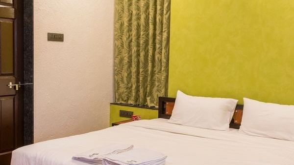 A close up shot of  wooden bed frame, white linens, a lime green accent wall, and an air conditioning unit.