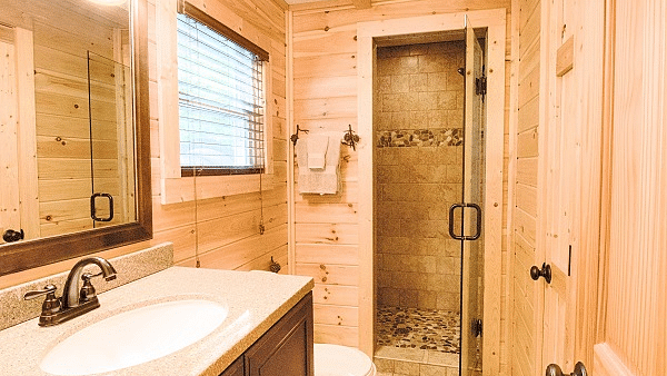 a shower cubical at the far end of the bathroom separated by a glass door with a wash basin and a commode beside it - Historic Tapoco Lodge