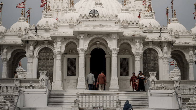 Ornate white Jain temple with intricate carvings, domes, and spires, featuring visitors ascending the grand entrance staircase.