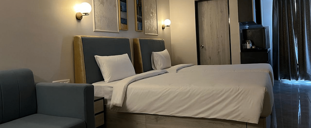 A side view of the spacious room featuring twin beds, a wall-mounted night lamp, and a photo frame above the headboard at Urban Suites by BluSalzz, Jaipur.