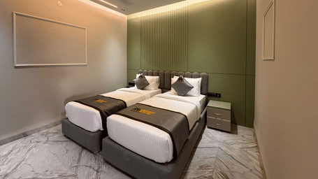 A wide angle shot of the Deluxe Twin Room featuring an olive green master wall and a set of twin beds sharing the wall at Hotel Mumbai House, Pithampur.