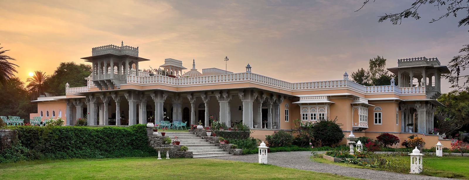 facade image of dev shree, deogarh with a beautiful lawn in the foreground and a picturesque sunset in the background