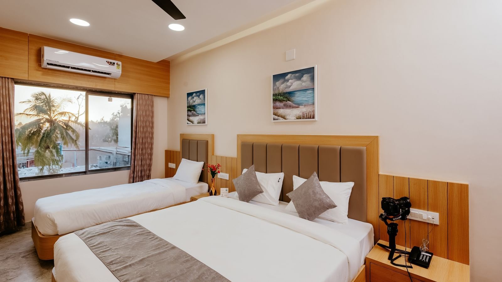 Corner view of a spacious Pride Room at Daksh The Grand Gowardhan, Dwarka, with multiple beds, modern decor, and a window with views.