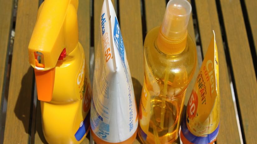 A close up of four different types of sunscreen on different types of bottles kept on a bench.