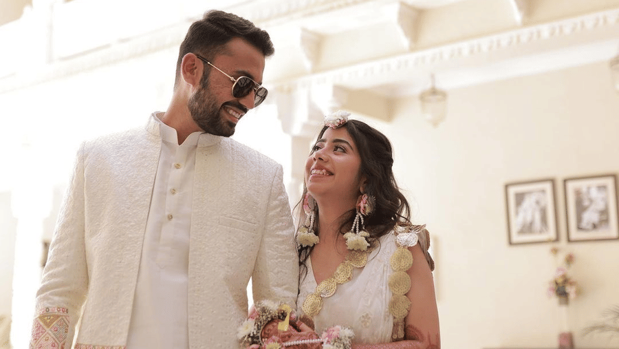 A bride and groom in white wedding attire look at each other in front of a white building at Amantra Shilpi Resort, Udaipur.