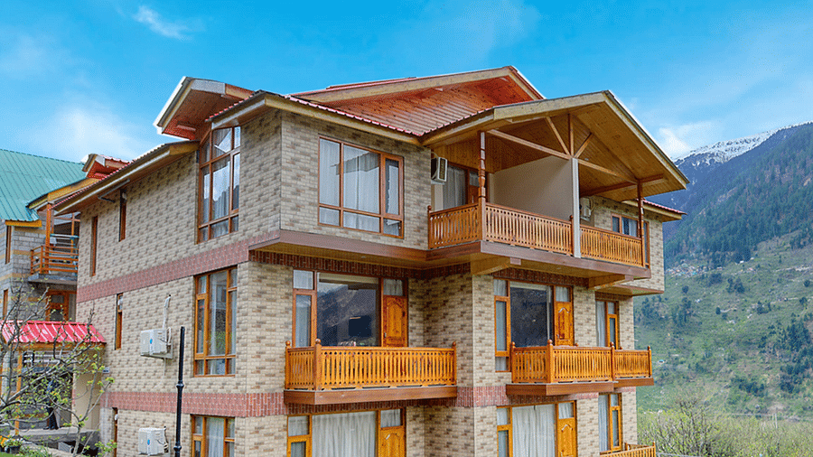 Facade of Clarks Inn Suites in Manali with lawn surrounding the bulding under clear blue sky with mountains in the background