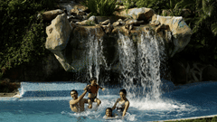 A group of four relaxing in a pool under a waterfall at The Retreat Hotel and Convention Centre.