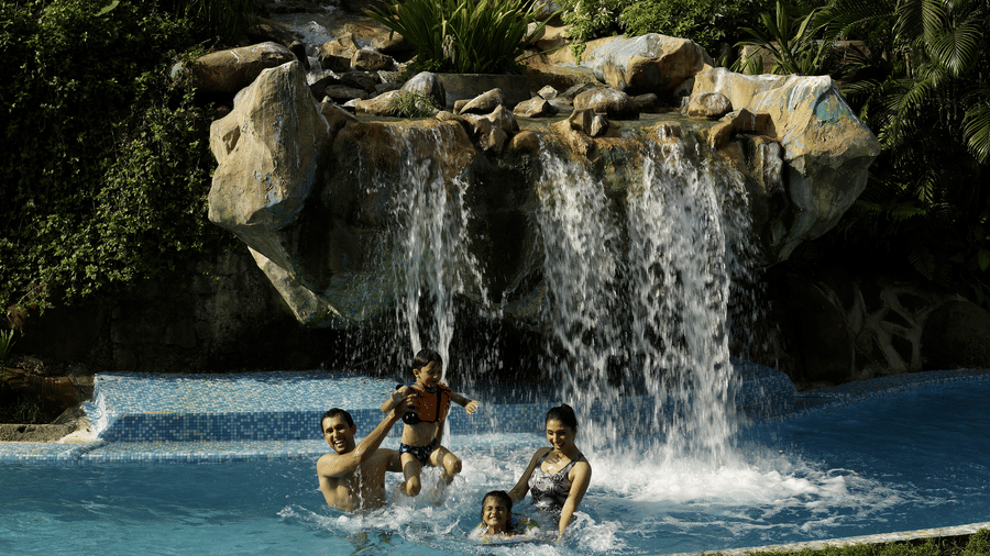 A group of four relaxing in a pool under a waterfall at The Retreat Hotel and Convention Centre.