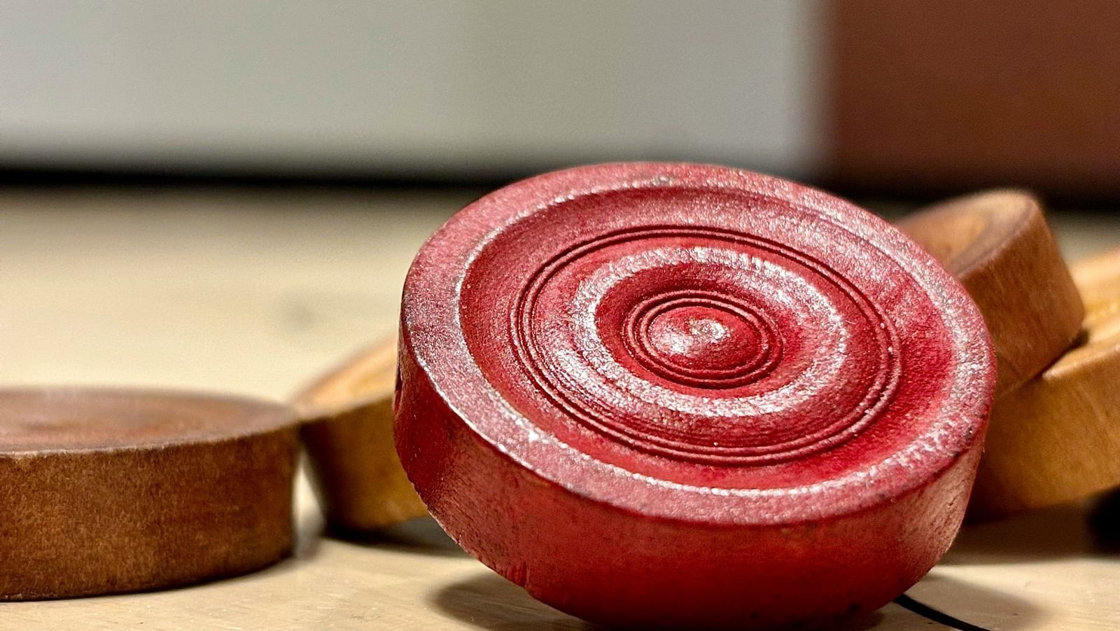 A red carrom man placed on beige carrom men on a carrom board.