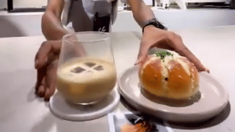 Barista presenting a freshly prepared coffee and a gourmet pastry on a plate at a curated cafe experience.