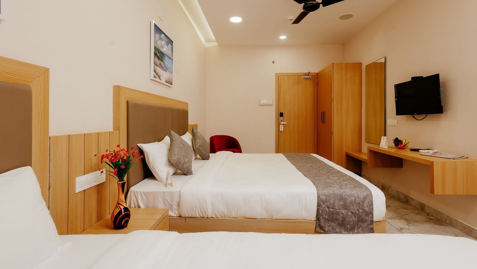 A well-furnished bedroom at Daksh The Grand Gowardhan, Dwarka, featuring comfortable beds and a wall mounted flat-screen television.