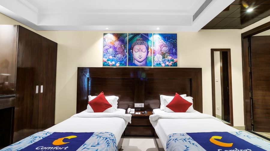 Room with twin beds, dark wood headboards, wardrobe, and framed artwork above the beds at Inde Reva Resorts Rishhikesh .