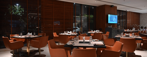A contemporary dining area with round tables and orange chairs set against a warm, wooden backdrop.