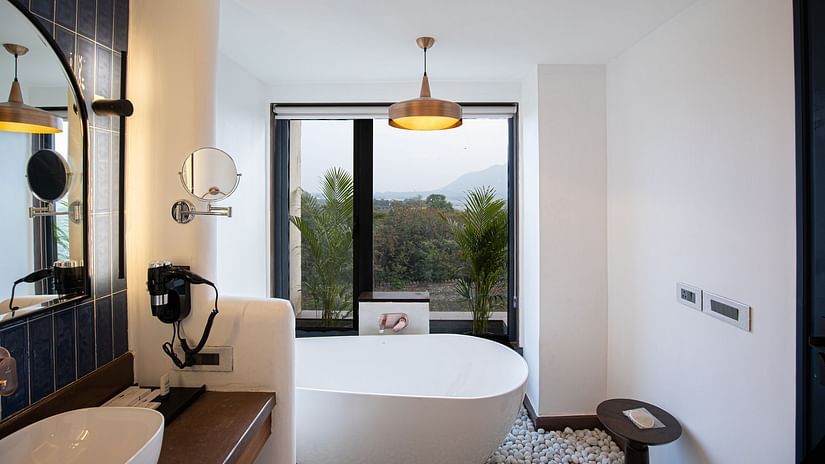 A bright washroom with a white tub, pebble floor, and a scenic window.