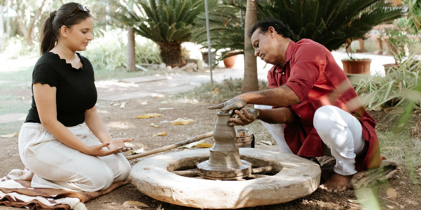 A woman and a man crafting pottery on a spinning wheel outdoors, with greenery in the background at Daksh Resort & Amusement Park.