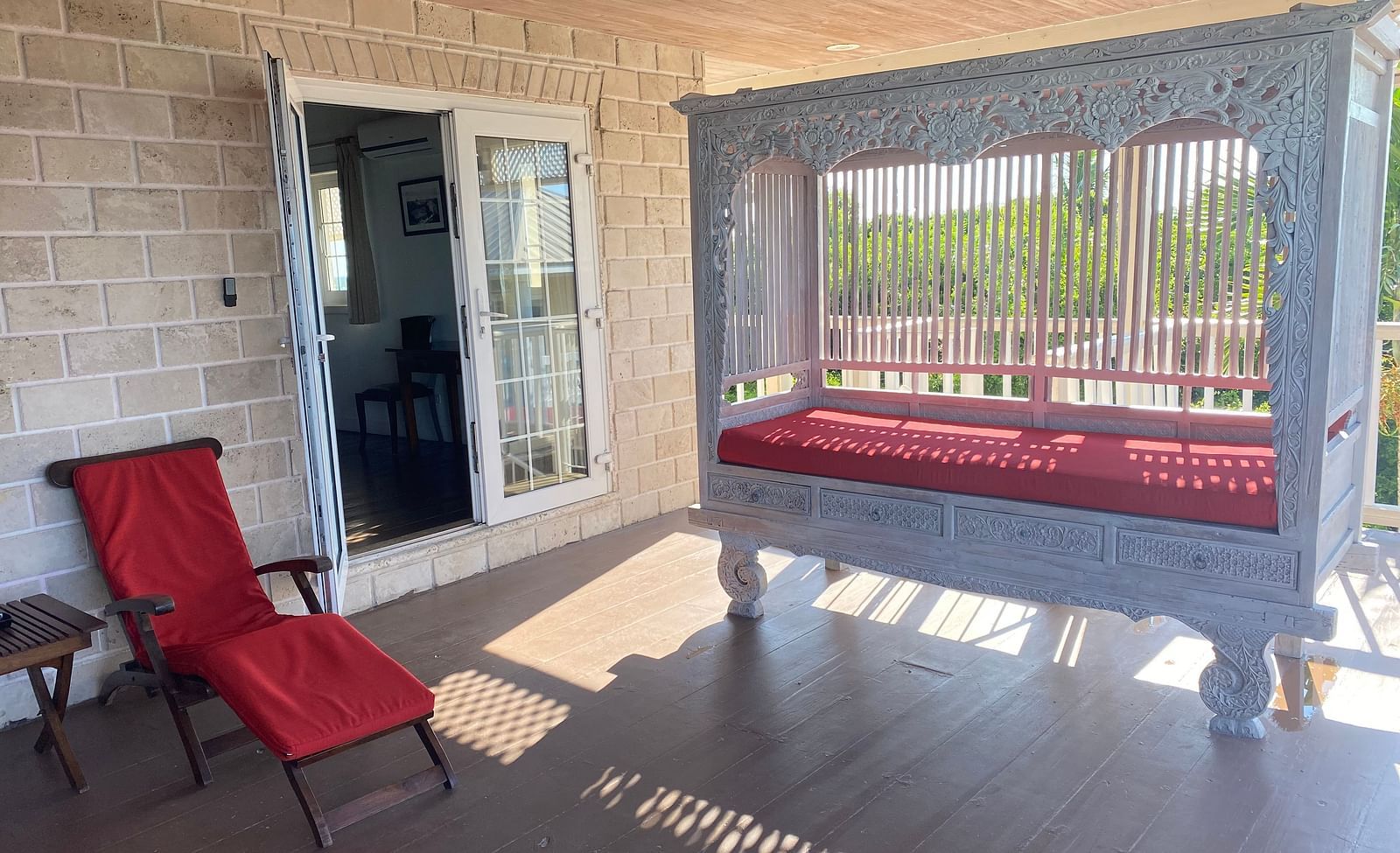 Veranda with red lounge chairs and sunlight streaming through white railing | A Stone's Throw Away