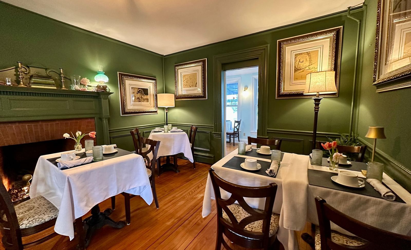 A dining room at Hartstone Inn featuring green walls, white tablecloths, and framed artwork