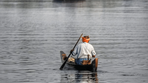 man rowing the boat with houseboat in the background