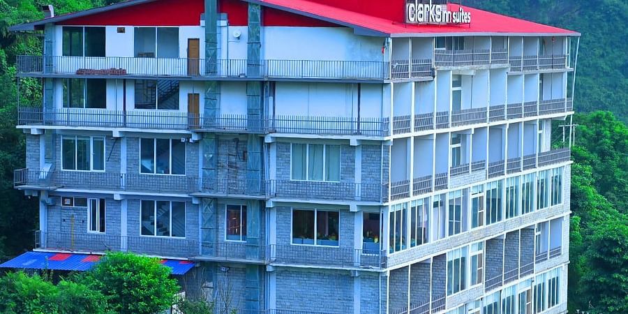 Facade of SPT Clarks Inn Suites, Mandi amidst lush greenery with a glimpse of a mountain in the bakcground