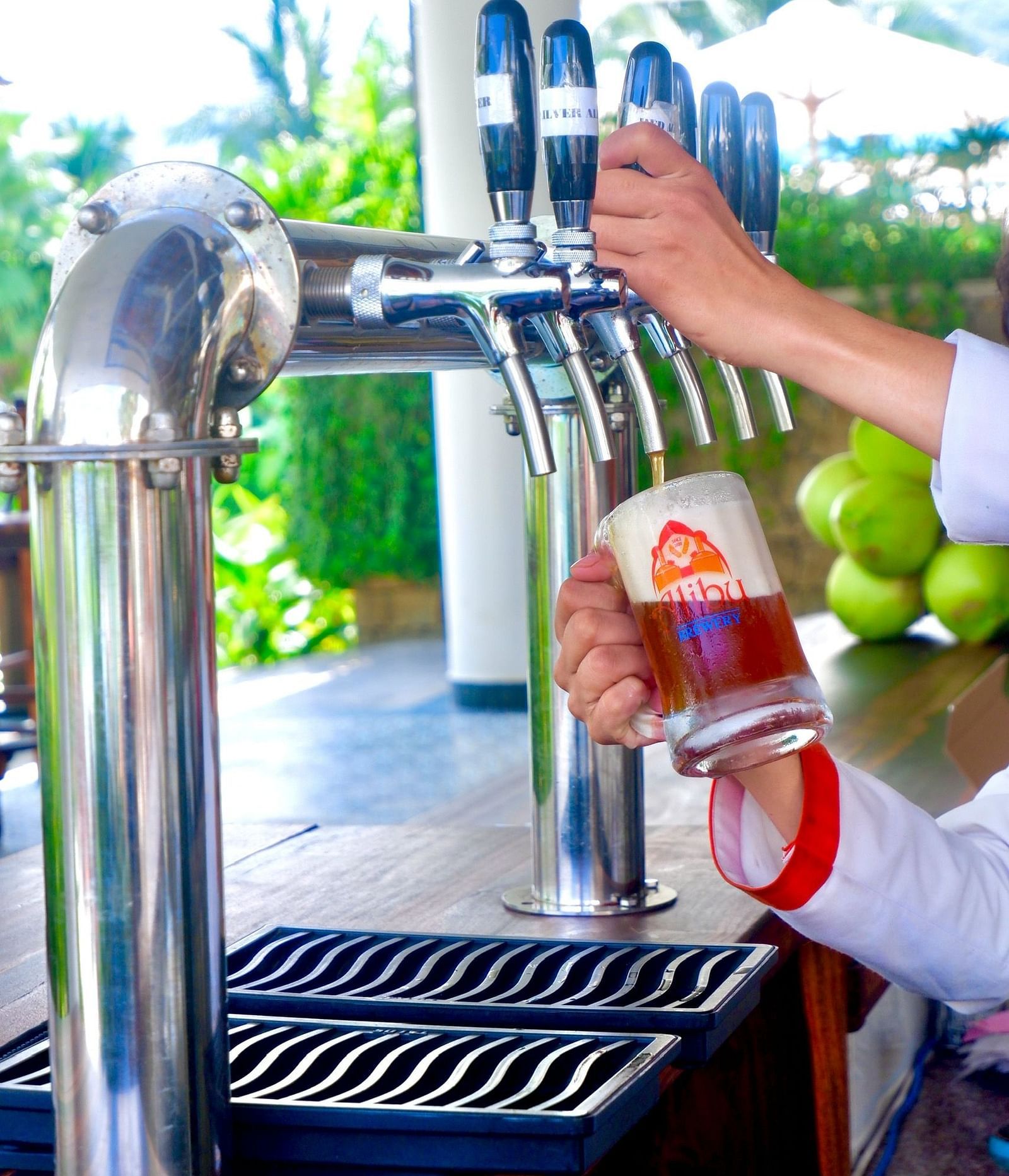 A person filling up a beer in a glass with the logo of the hotel on it - Alibu Resort Nha Trang