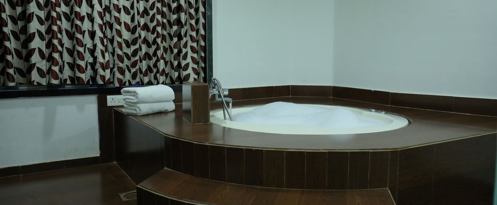 A corner of a washroom in a suite of Krushnai Resort showcasing a large, Jacuzzi with surrounding wooden steps.
