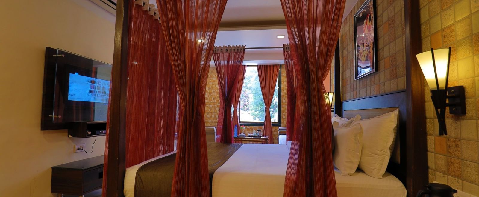 A suite at Krushnai Resort, featuring a four-poster bed draped in red and warm lighting.