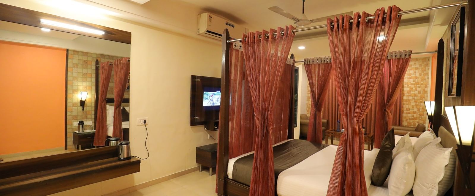 A spacious suite at Krushnai Resort with a four-poster bed, a mirror on the wall, and long red drapes hanging above the posters of a king size bed.