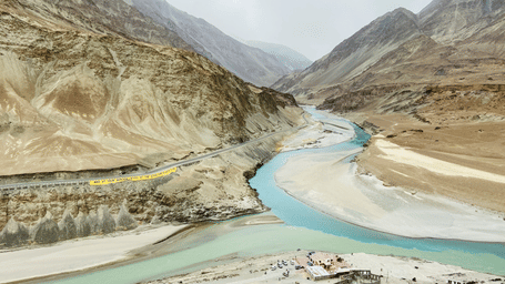 A high-angle view showing the confluence of 2 rivers winding through a vast mountain valley.