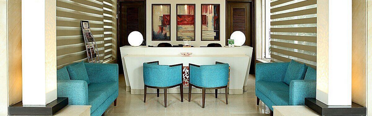 A reception area featuring stylishly arranged furniture, wall-mounted photographs, and a chandelier hanging from the ceiling at Inde Signature Tower, Gurgaon